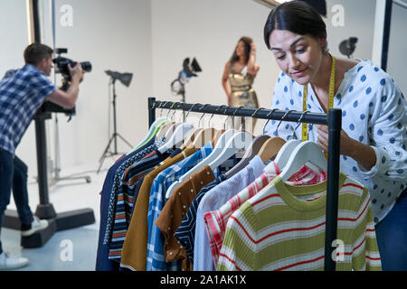 Stylist Choosing Clothes For Fashion To Wear On Photo Shoot In Studio Stock Photo