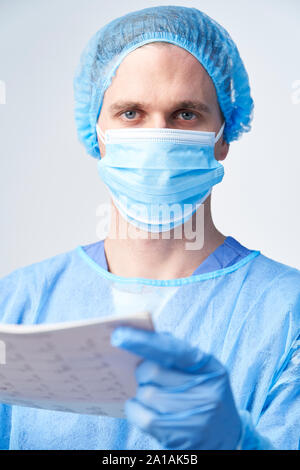 Studio Portrait Of Male Surgeon Wearing Gown And Mask Holding Medical Print Out Stock Photo