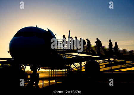 Silhouette of airline passengers boarding airplane at sunrise Stock Photo