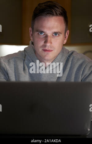 Portrait Of Suspicious Looking Man Using Laptop In Evening At Home Stock Photo