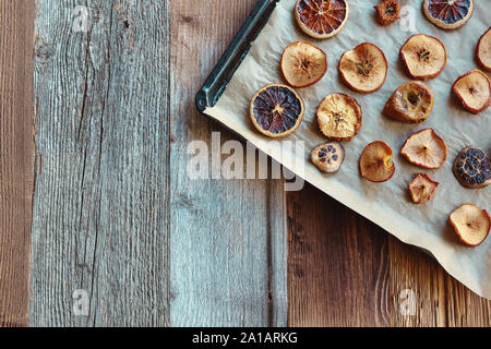 Homemade slices of dried oranges and apples on baking paper and black baking tray, diagonal arrangement from top right corner, top down, copy space Stock Photo