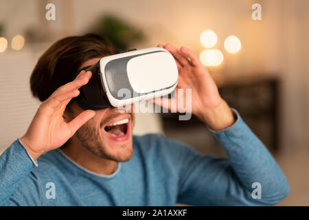 Millennial Guy Using Virtual Reality Glasses Playing Videogame At Home Stock Photo