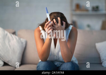 Unrecognizable Depressed Girl Holding Pregnancy Test Sitting On Couch Indoor Stock Photo