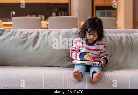 Little girl sitting on her sofa using a digital tablet