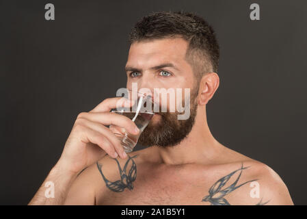 man with beard on face drink water from glass on grey background, healthcare and life source, hangover and thirst, refreshing Stock Photo