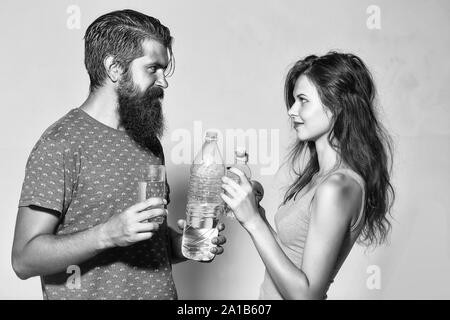 Attractive couple of beautiful long-haired girl and handsome bearded man with water bottles glass and apple look at each other on grey wall Stock Photo