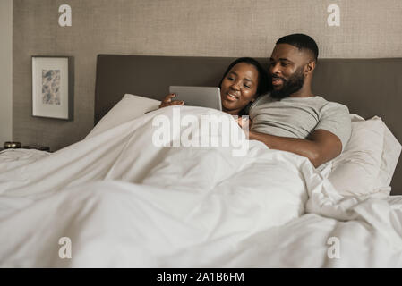 African American couple watching videos on a tablet in bed Stock Photo