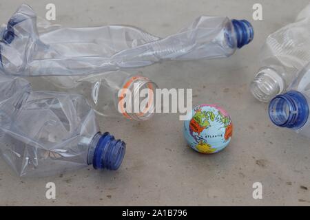 Pet plastic bottles pointing at planet earth globe on grey surface. Showing plastic pollution, recycling and zero waste concepts. Stock Photo