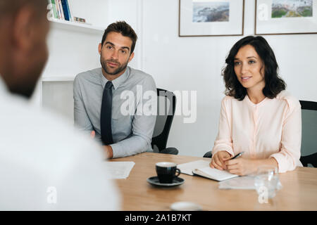 Two young businesspeople talking with a colleague in an office Stock Photo