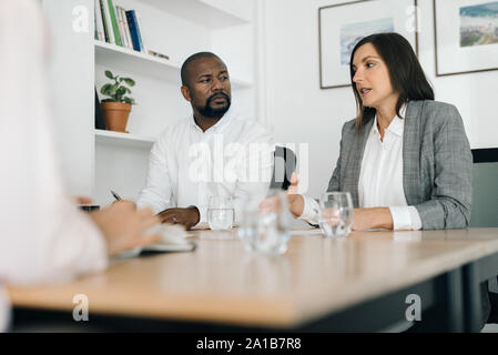 Two businesspeople talking with a colleague at an office table Stock Photo