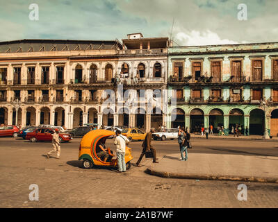 Havana, Cuba - September 2019: Vintage car and colonial houses build next to each other. Bright colour facade and vintage taxi vehicle in the streets Stock Photo