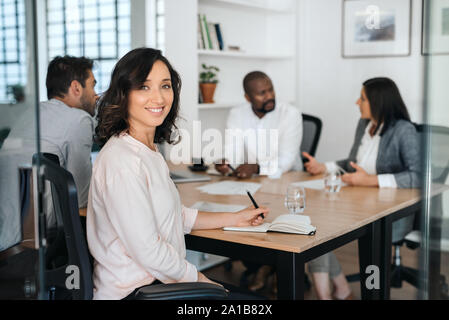 Smiling young businesswoman sitting with coworkers during a meeting Stock Photo