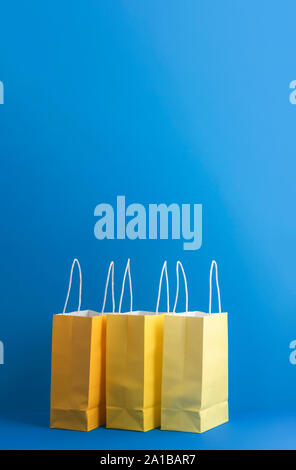 Three yellow paper bags on blue background with negative space. Yellow shopping bags. Christmas gift shopping concept. Presents paper bags. Stock Photo