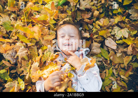 little toddler girl laying on the ground in yellow leaves
