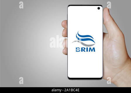 A man holds a smartphone displaying the logo of company Brim listed on Nasdaq Iceland. Grey gradient in the background. Credit: PIXDUCE Stock Photo