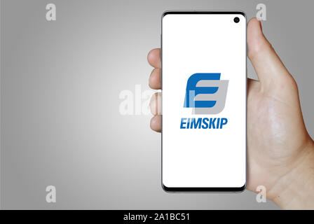 A man holds a smartphone displaying the logo of company Eimskipafélag Íslands listed on Nasdaq Iceland. Grey gradient background. Credit: PIXDUCE Stock Photo