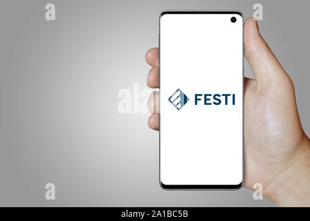 A man holds a smartphone displaying the logo of company Festi listed on Nasdaq Iceland. Grey gradient in the background. Credit: PIXDUCE Stock Photo