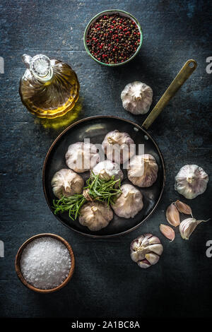 Garlic cloves and bulb in pan with fresh rosemary olive oil salt and spice on concrete table Stock Photo