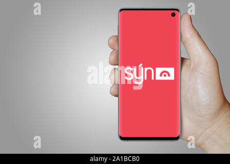 A man holds a smartphone displaying the logo of company Sýn listed on Nasdaq Iceland. Grey gradient in the background. Credit: PIXDUCE Stock Photo