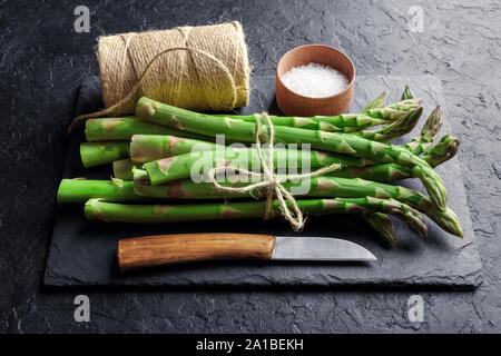 Green asparagus sprout with knife, salt and rope on black plate Stock Photo
