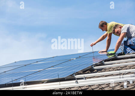 Installing solar photovoltaic panel system. Solar panel technician installing solar panels on roof. Alternative energy ecological concept. Stock Photo