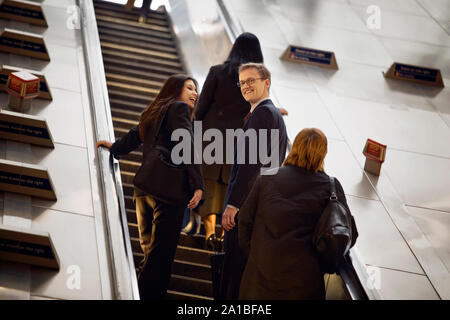 Portrait of a smiling businessman standing on an escalator with his colleagues. Stock Photo