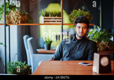 Confident young indian man in black shirt sitting at cafe. Stock Photo