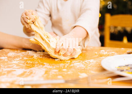 Detail of toddler hands kneading and stretching dough on wooden table Stock Photo