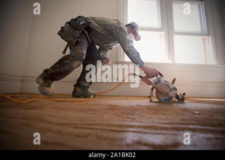 Male builder sanding floorboards with a power tool inside a room. Stock Photo
