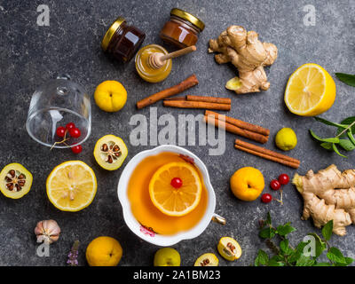 backgroundof cup of ginger tea with lemon, cranberry, different honey in jars, cydonia, cinnamon sticks on concrete background Stock Photo