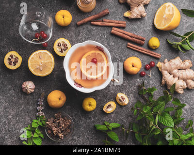 backgroundof cup of ginger tea with lemon, cranberry, different honey in jars, cydonia, cinnamon sticks on concrete background Stock Photo