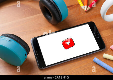 Carrara, Italy - September 25, 2019: Smartphone with Youtube Kids logo on wooden table next to a pair of wireless earphones, some pencils and some cha Stock Photo