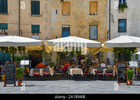 Outdoor restaurant in Piazza dell'Anfiteatro in the centre of Lucca with people and tourists having lunch under sun shades in summer, Tuscany, Italy Stock Photo