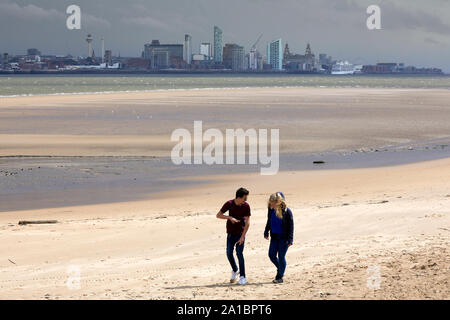 New Brighton beach Promenade, Wallasey. a young couple walking along the sand with Liverpool skyline behind Stock Photo