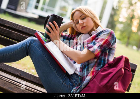 Tired female student fall asleep while drinking coffee and studying outdoor. Stock Photo