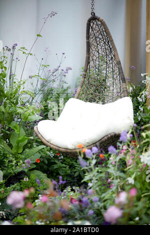 Modern luxury relaxing hanging chair seating made of wicker in a modern floral garden Stock Photo
