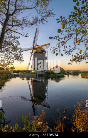 Serene view of a Dutch windmill reflected in the calm water of a polder canal at dusk. Rietveldse molen, Hazerswoude-Dorp, Netherlands Stock Photo