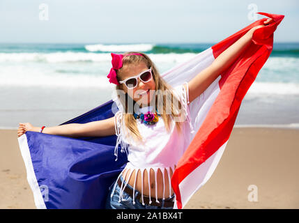 Happy French girl carries fluttering blue white red French flag of France against blue sky and Atlantic ocean background Stock Photo