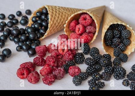 Three waffle cones close-up of which poured on the table raspberries, currants, blackberries Stock Photo