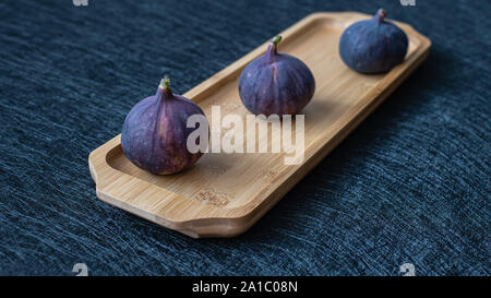 Three figs on a wooden tray on a black background close-up Stock Photo