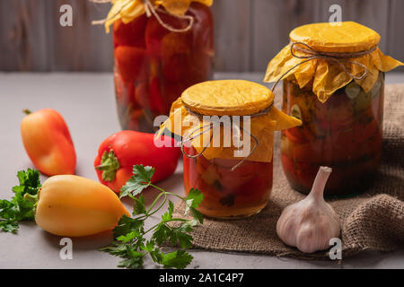 Homemade jars of pickled peppers and tomatoes on a rustic wooden background. Pickled and canned product. Next ingredients for cooking. Stock Photo
