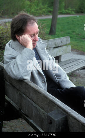 unhappy man sitting on park bench alone Stock Photo