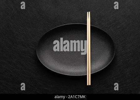 Empty oval black plate with chopsticks on dark background. Japanese food style. Top view with copy space Stock Photo