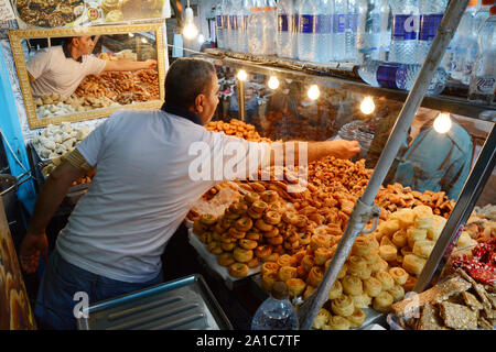 A food merchant selling biscuits and pastries serves a waiting customer in the market of the kasbah, in the medina of Tunis, Tunisia. Stock Photo