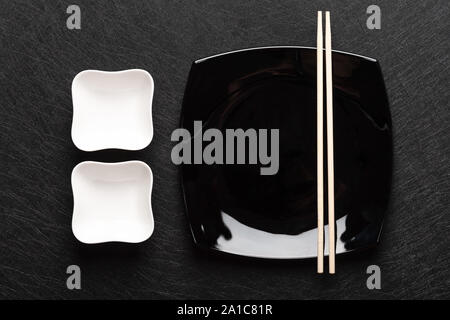 Empty black plate with chopsticks and two white gravy boats on a dark background. Japanese food style. Top view  Stock Photo