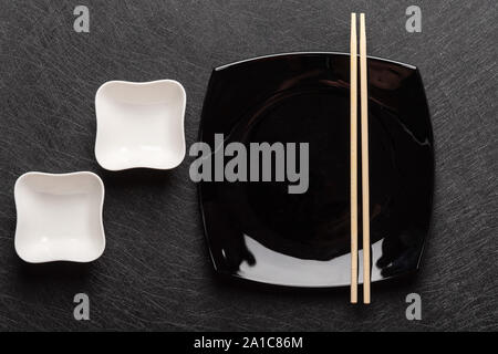 Empty square black plate with chopsticks and two white gravy boats on a dark background. Japanese food style. Top view  Stock Photo