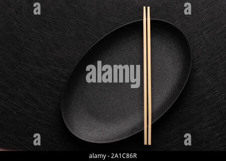 Empty oval black plate with chopsticks on dark background. Japanese food style. Top view with copy space Stock Photo