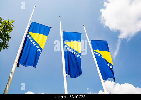 Three bosnian flags in wind on blue sky with clouds Stock Photo