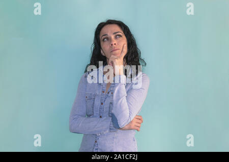 Brunette woman with her hand on her chin, thinking about some question, isolated on a blue background Stock Photo