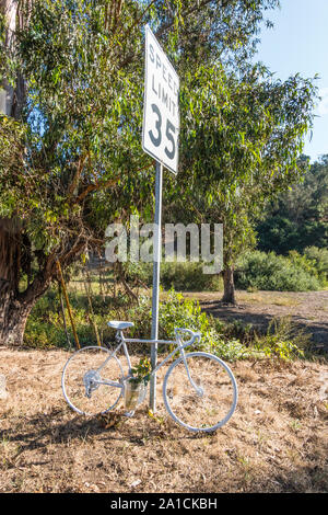 Roadside memorial to a bikers death with a bicycle painted all white, flowers and a vase on the side of Modoc Road in Santa Barbara, California. Stock Photo